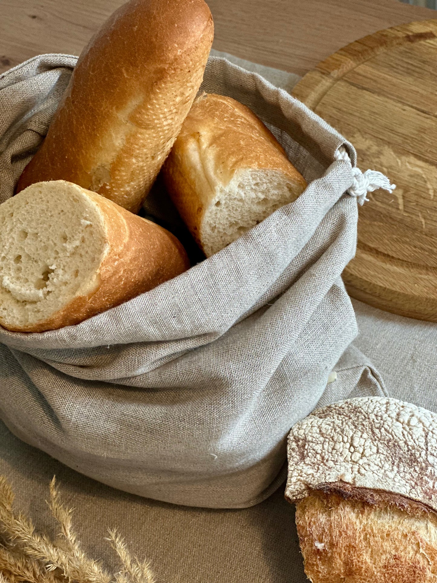 Three loaves of bread in the Kolo Pechi linen bread bag on a wooden surface