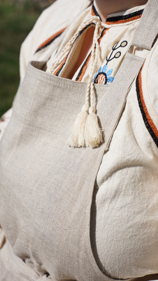 A part of the Kolo Pechi linen apron on a woman wearing an embroidered dress underneath  