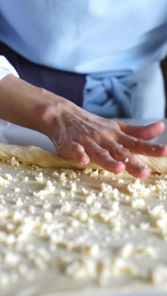 A person wearing the Kolo Pechi light blue Bib Apron working with dough and cottage cheese cooking Bessarabian Milinaa