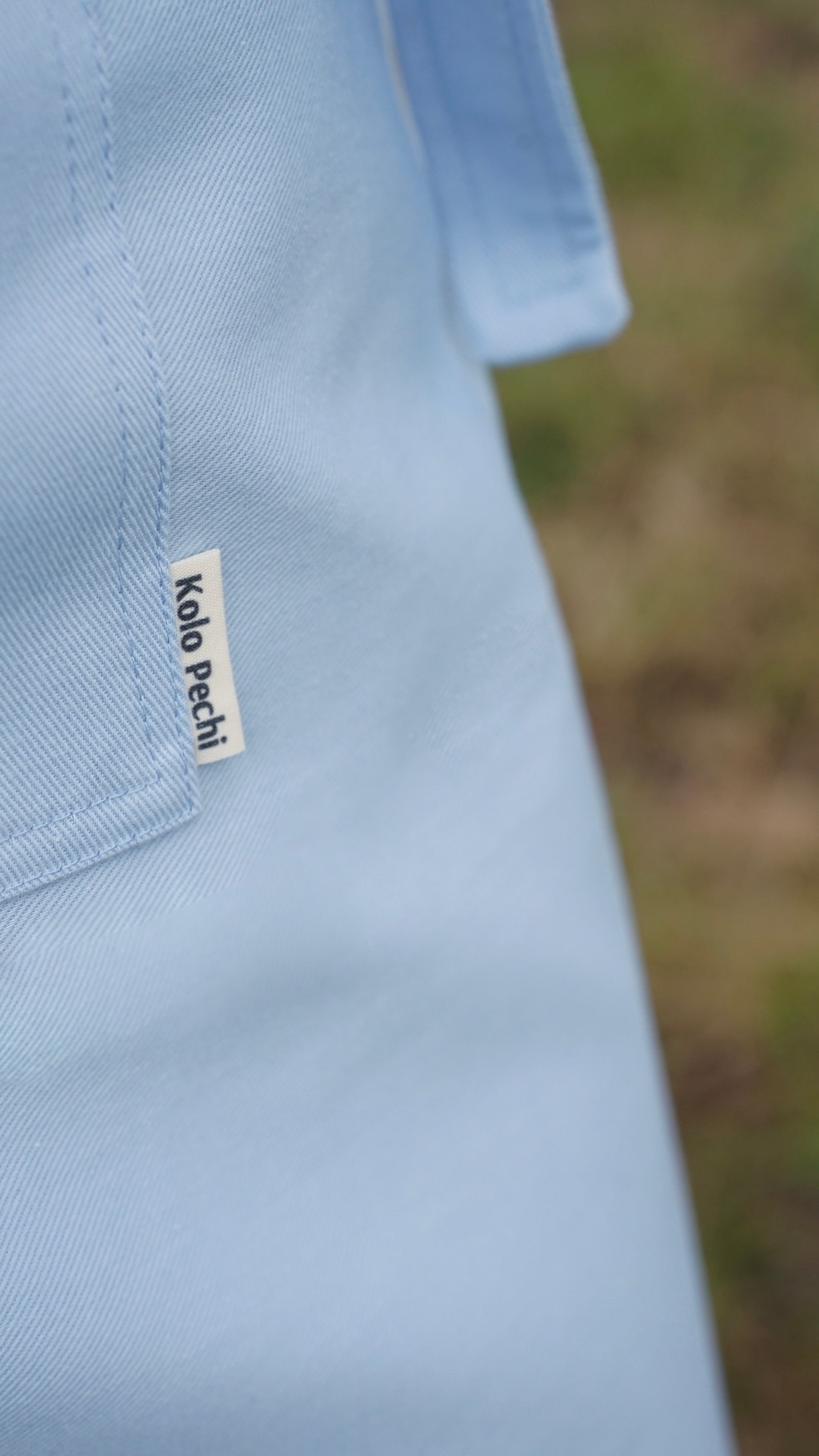 Light blue apron with a visible brand label on a blurred natural background