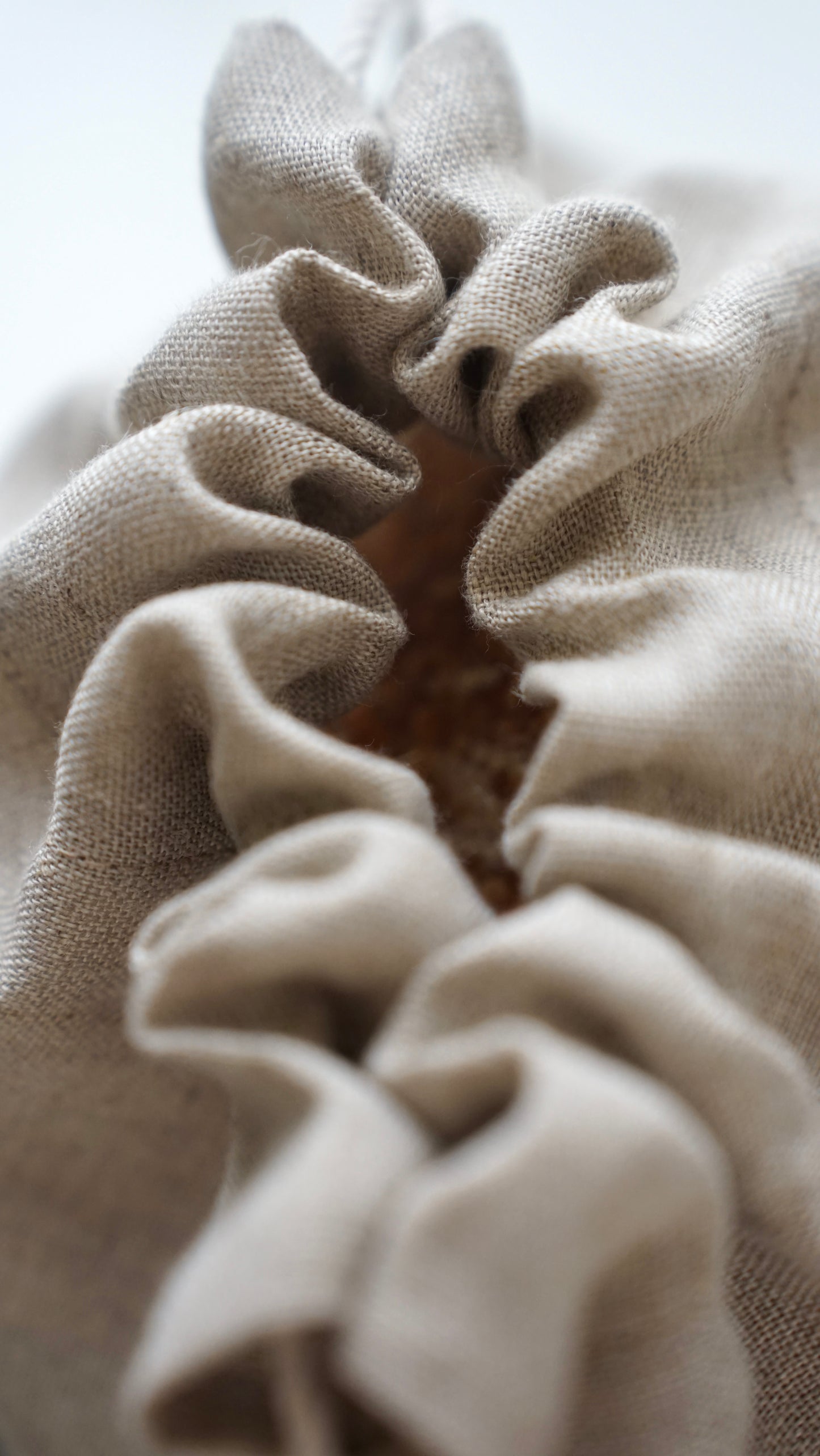Close-up of a beige linen bread bag with gathered ruffles and a visible bread inside opening.