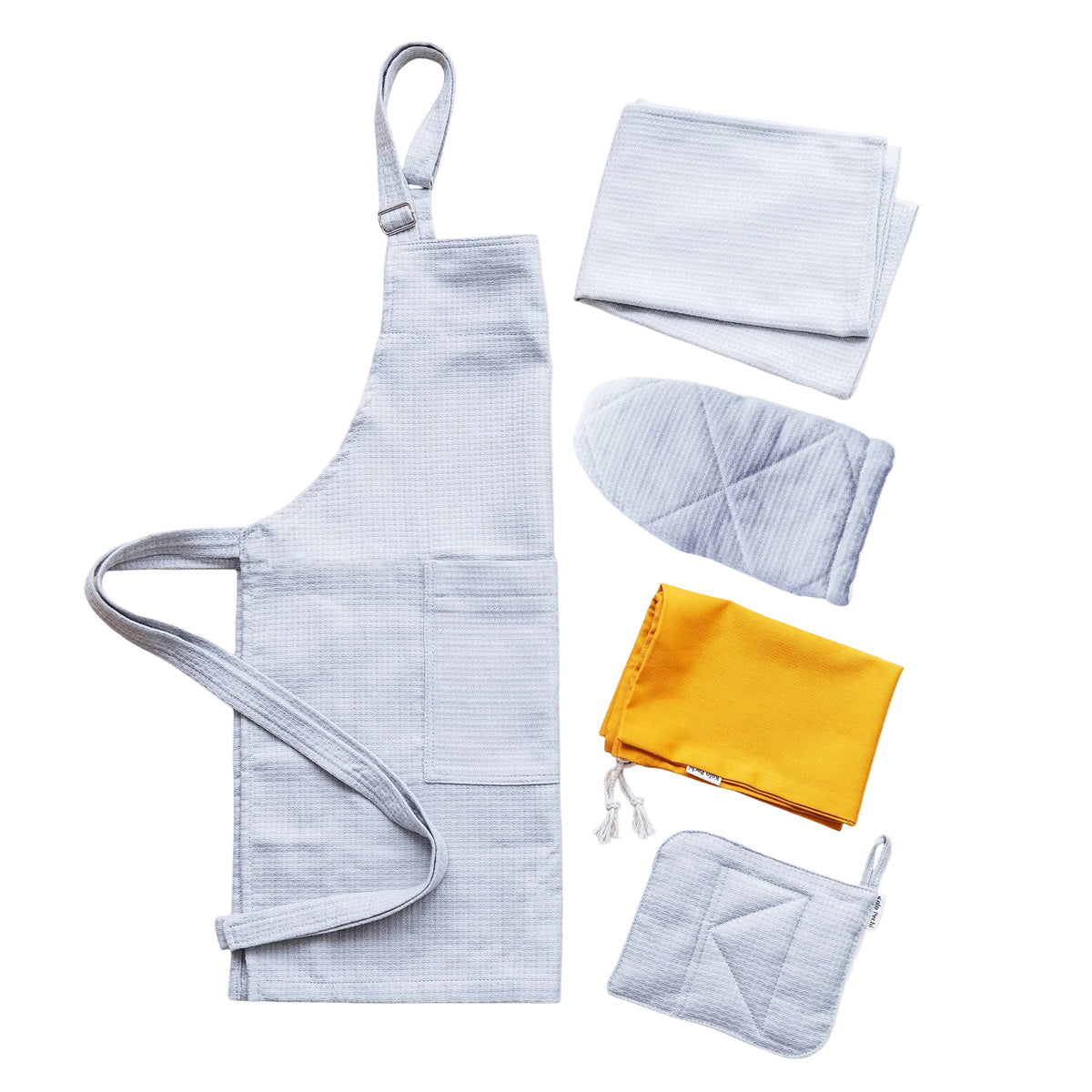 A flat-lay product shot of The Lviv Sky set of kitchen textiles on a light gray background. The set includes a gray Kolo Pechi cotton apron, matching folded towel, a quilted oven mitt, a folded mustard yellow grocery bag, and a quilted pot holder .