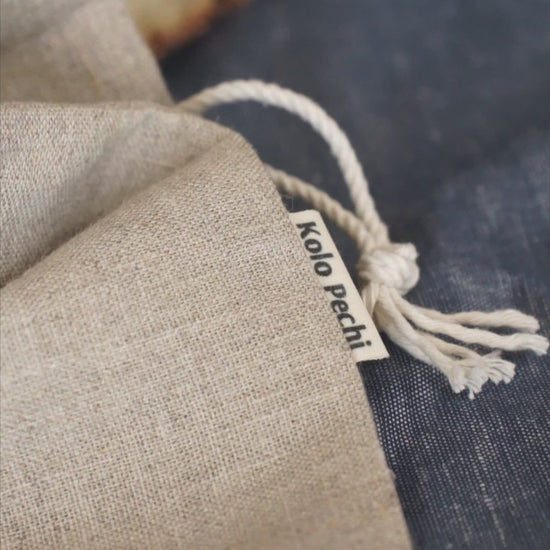 The Kolo Pechi linen bread bag with a loa of bread in it on the linen tea towel